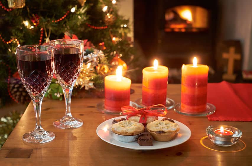 A Christmas tree scene at night with glasses of wine,mince pies, lit candles and fire.